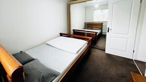 Un dormitorio pequeño y acogedor con una cama individual, cabecera de madera, un espejo grande y una puerta blanca.