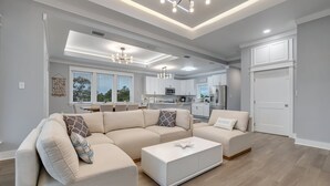 A modern living room with a sectional sofa, a coffee table, and a kitchen in the background. - Modern Oceanview Vacation Home (Saint George Island)