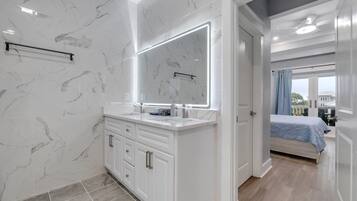 A modern bathroom with marble tiles, a large mirror, and a walk-in shower.