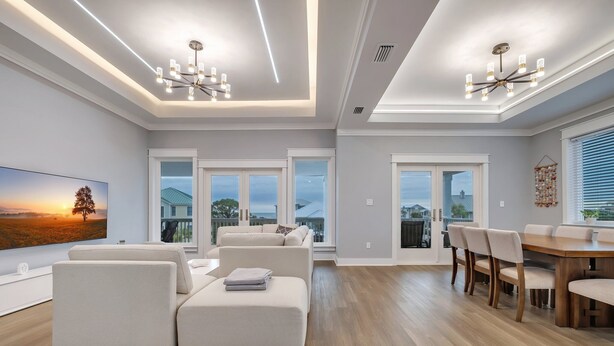 A modern living room with a sectional sofa, a dining table with chairs, and a large window offering a view of the outdoors. - Modern Oceanview Vacation Home (Saint George Island)