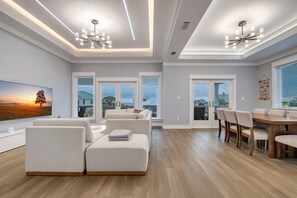 A modern living room with a sectional sofa, a dining table with chairs, and a large window offering a view of the outdoors. - Modern Oceanview Vacation Home (Saint George Island)