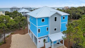 A multi-story building with a blue and white exterior, surrounded by trees and a clear sky. - Modern Oceanview Vacation Home (Saint George Island)