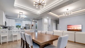 A modern kitchen with white cabinetry, a wooden dining table, and a large island with bar stools. - Modern Oceanview Vacation Home (Saint George Island)