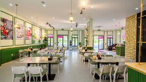A spacious restaurant with green walls, white chairs, and tables. There are posters on the walls and a bar area in the background. - Osen Hotel - Grand World Phu Quoc (Phu Quoc)