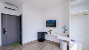 A modern hotel room with a wooden floor, a desk with a phone and decorative items, a painting on the wall, and a door with a handle. - Osen Hotel - Grand World Phu Quoc (Phu Quoc)