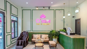 A reception area with a green reception desk, a massage chair, a sofa, and a small table with a tray. - Osen Hotel - Grand World Phu Quoc (Phu Quoc)