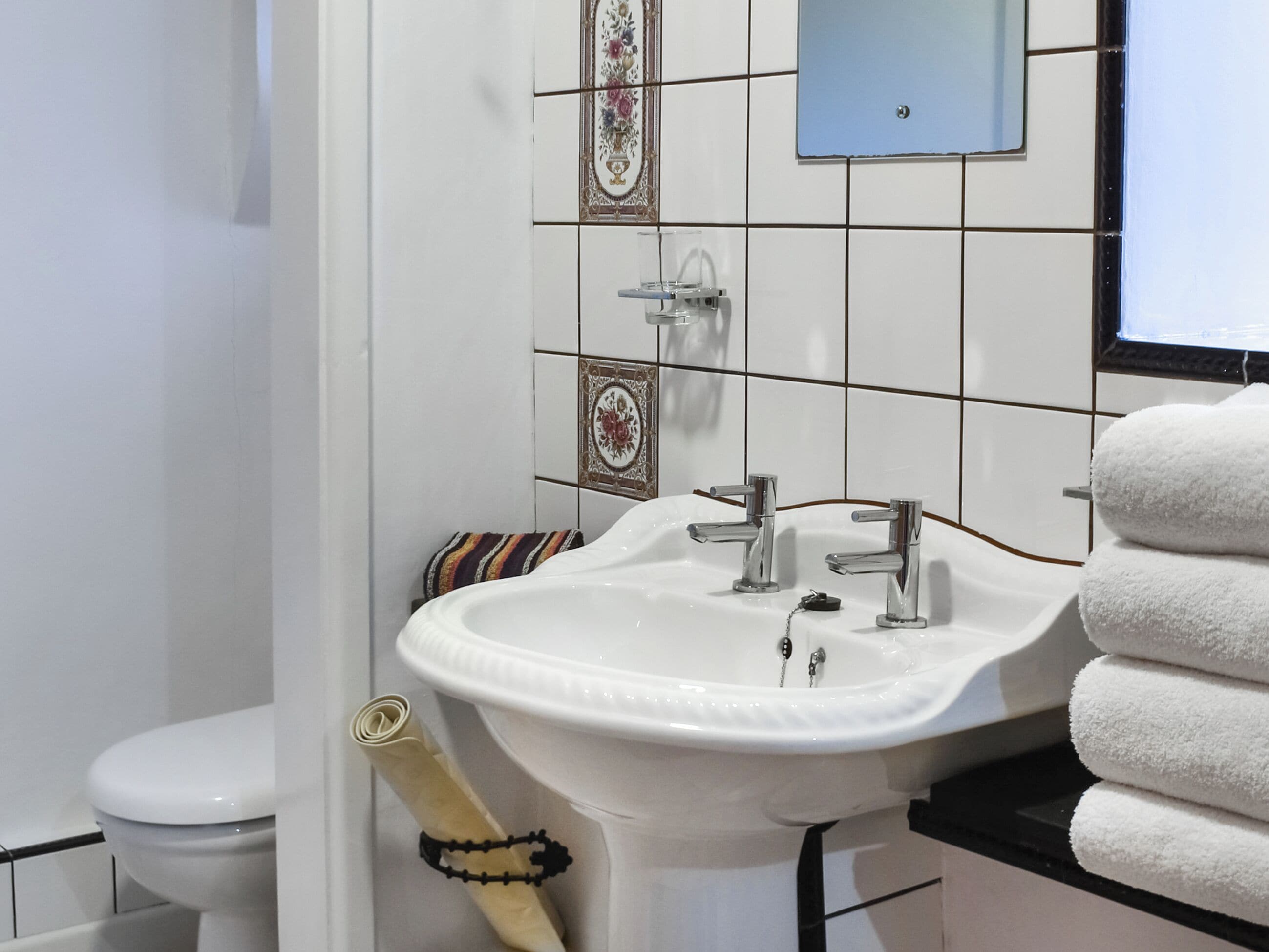 A bathroom with a white sink, two faucets, a toilet, and a towel rack with a towel.