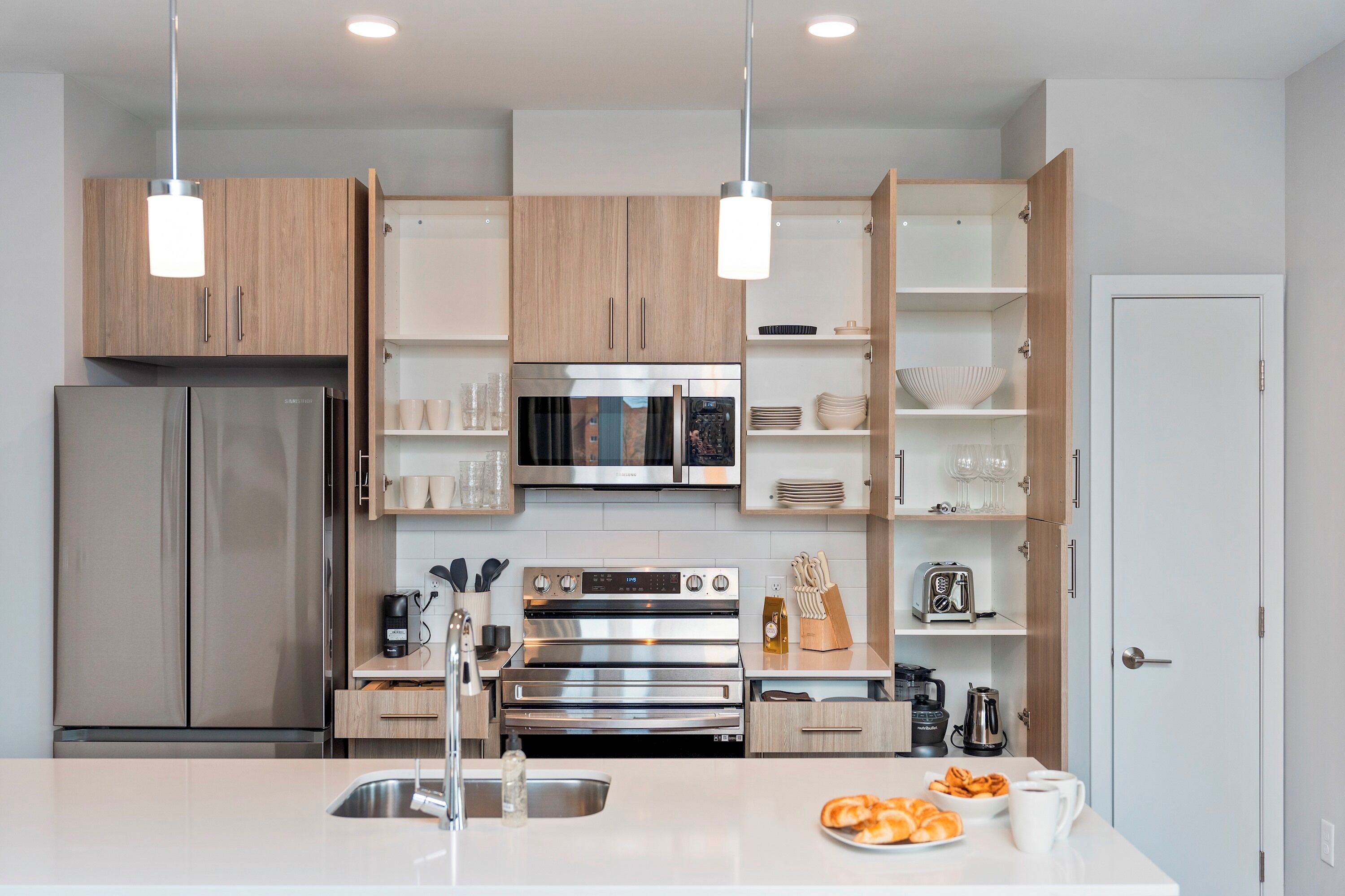 A modern kitchen with stainless steel appliances, wooden cabinets, and pendant lighting.