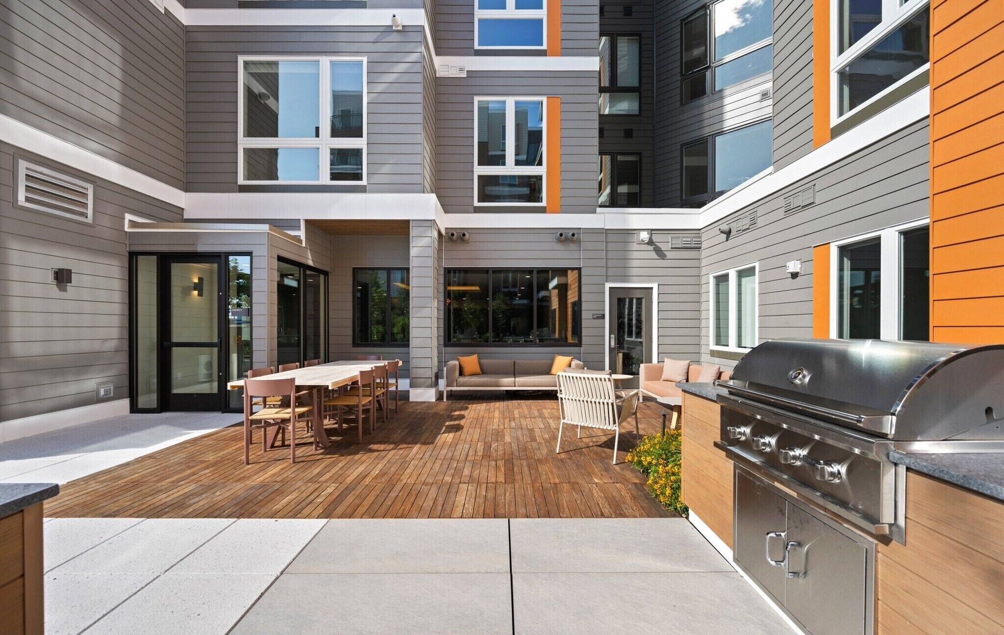 Une terrasse extérieure moderne, dotée d’une plateforme en bois, d’un barbecue et d’un espace détente avec un canapé et des fauteuils.
