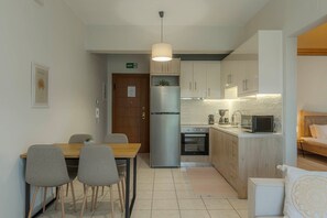 A compact kitchen with a dining area, featuring a refrigerator, oven, microwave, and a small coffee maker. - Aria Guest Residence, Apartment (Galatas)