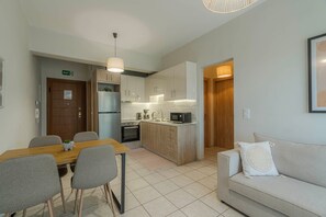 A modern kitchen with white cabinets, a built-in oven, and a microwave. There is a dining area with a wooden table and chairs.