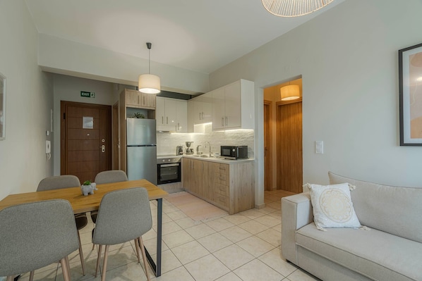 A modern kitchen with white cabinets, a built-in oven, and a microwave. There is a dining area with a wooden table and chairs.