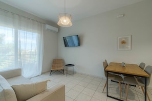 A modern living room with a sofa, a dining table with chairs, a television, and a pendant light.
