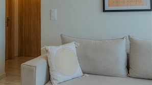 Una sala de estar con un sofá, una obra de arte enmarco y una puerta que da a otra habitación.