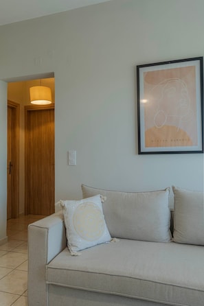 A living room with a sofa, a framed artwork, and a door leading to another room.