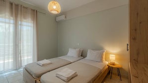 Habitación de hotel con dos camas, una ventana con cortinas, una lámpara colgante y una pequeña mesa con lámpara.