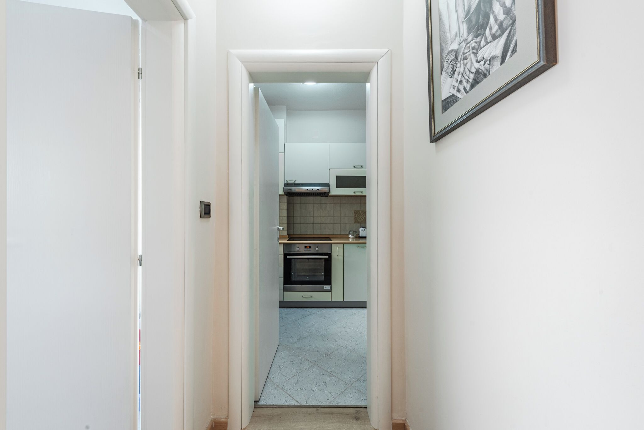 A narrow hallway leading to a kitchen with white cabinets, a microwave, and an oven.