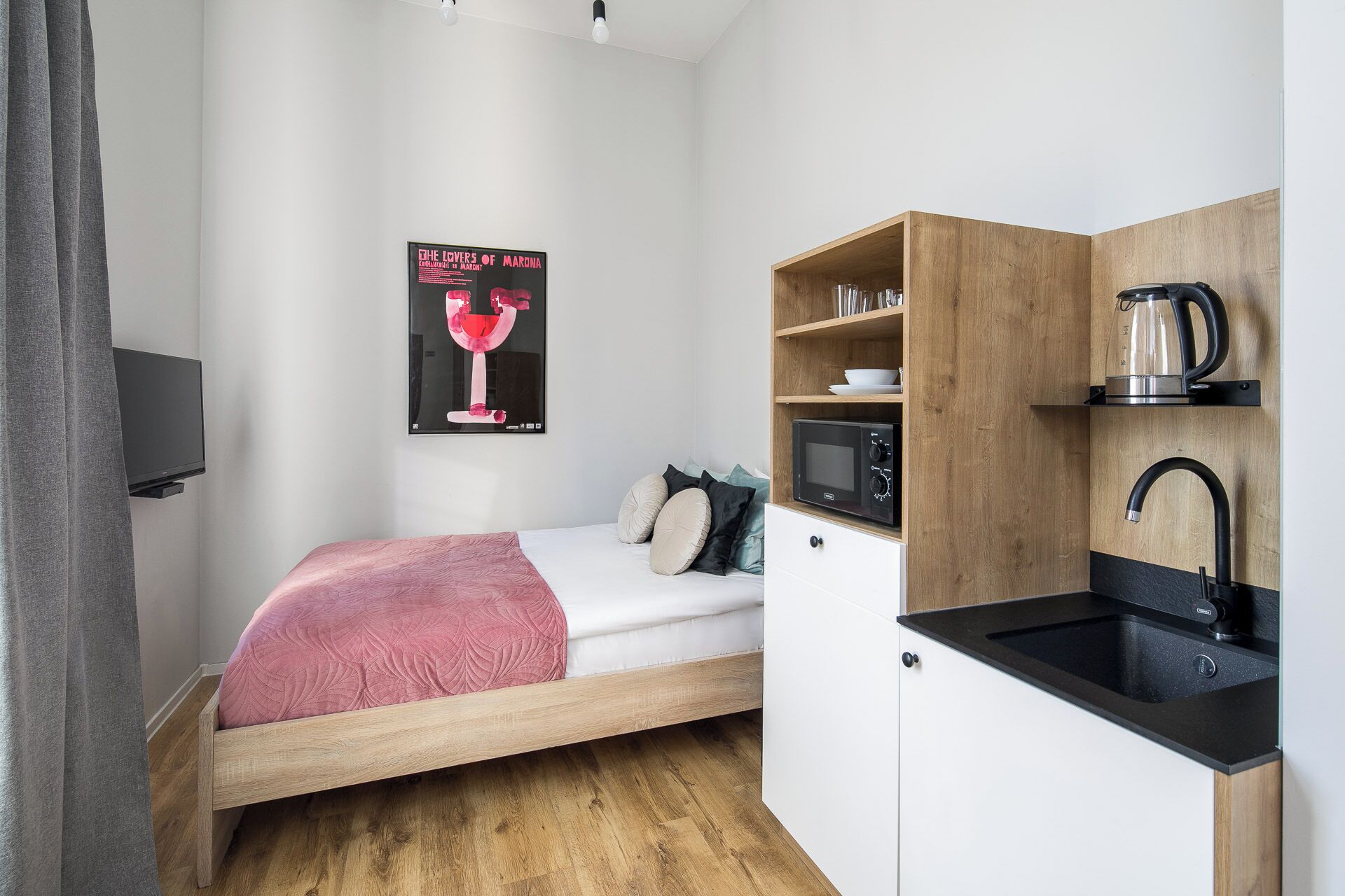 Een compacte kamer met een bed, een kleine kitchenette en een televisie aan de muur.