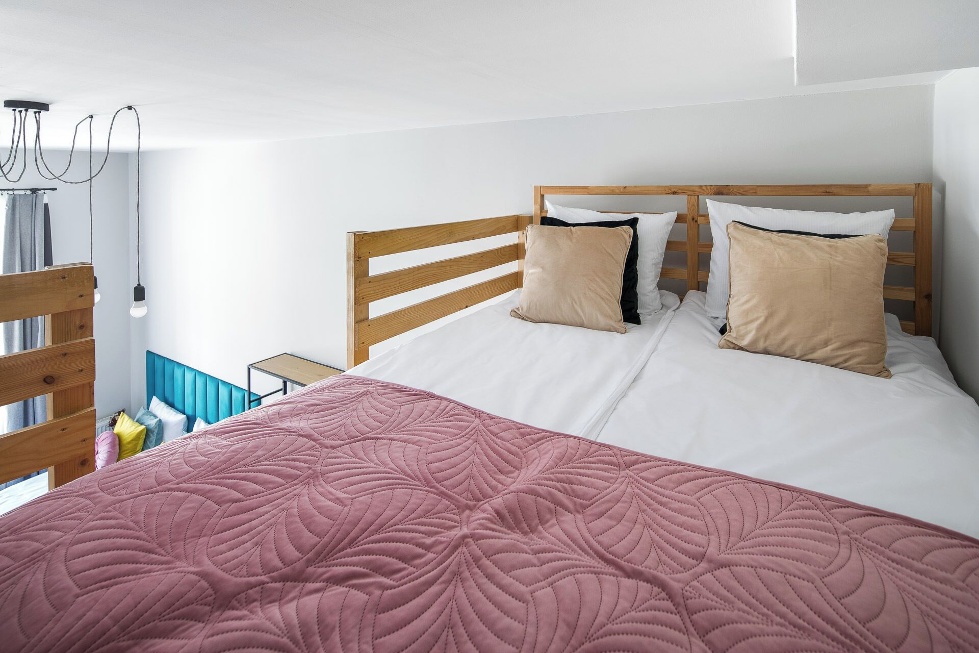 A bedroom with a wooden headboard, white bedding, and a pink quilted bedspread.