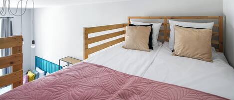 A bedroom with a wooden headboard, white bedding, and a pink quilted bedspread.
