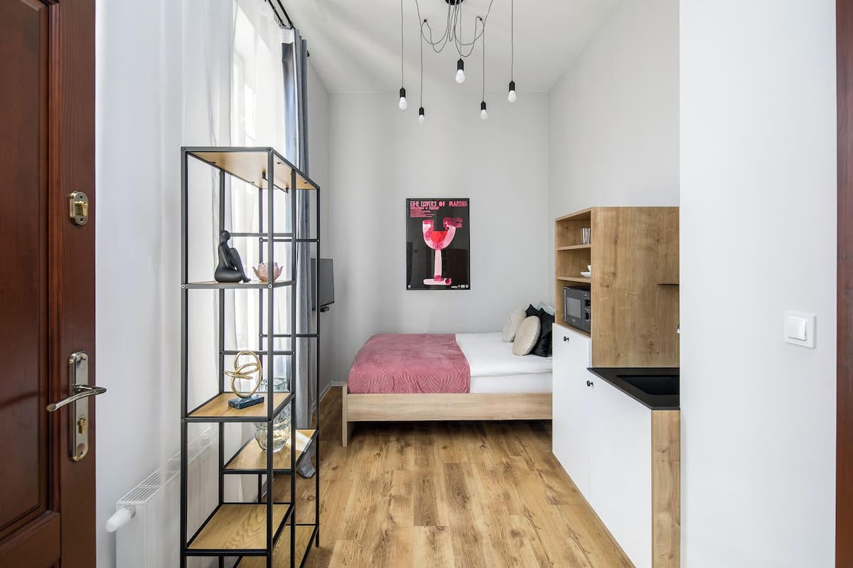 Un dormitorio compacto con cama, estantería de madera, un cartel en la pared y una pequeña cocina.