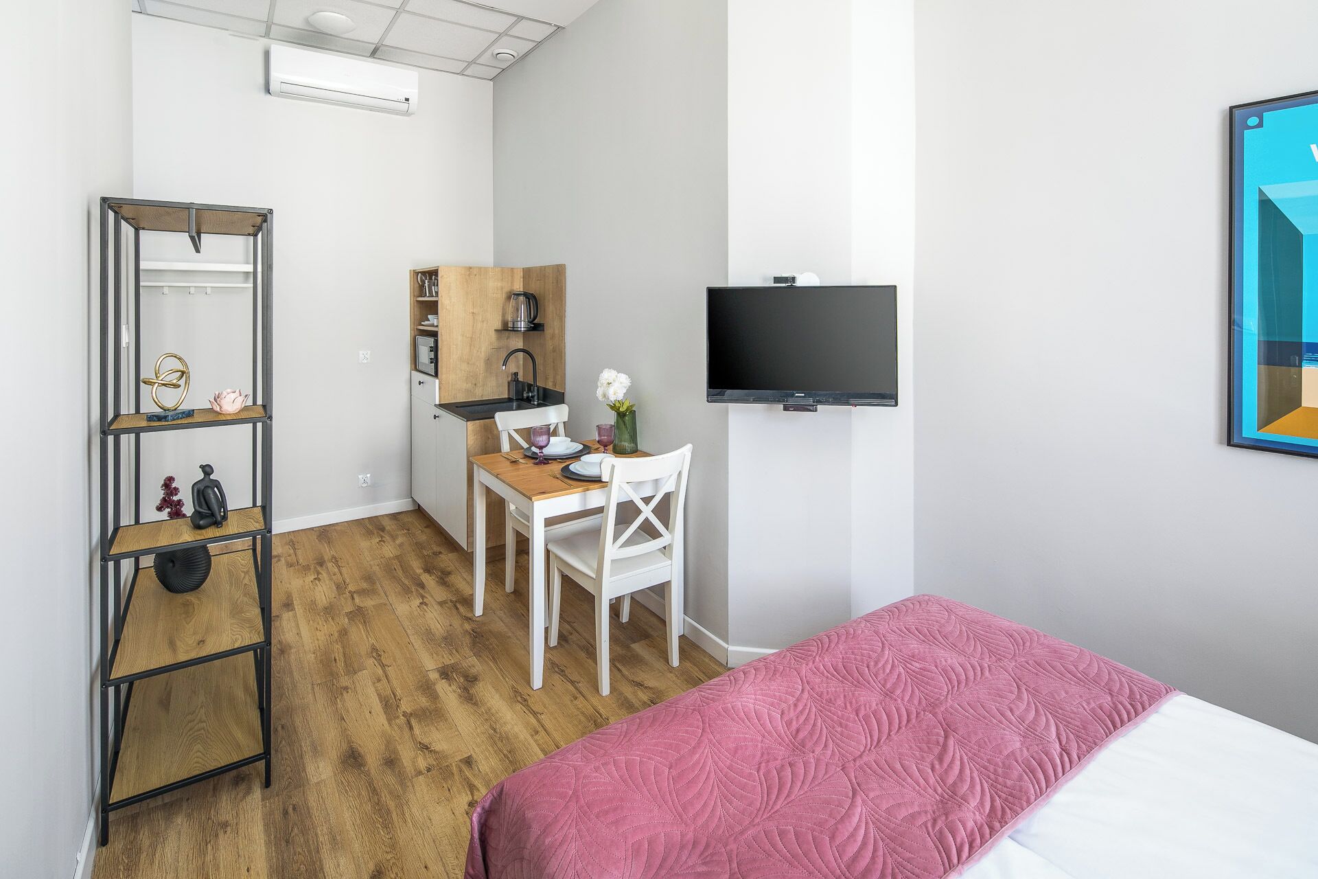 A compact room with a bed, a desk with a chair, a TV, and a shelf unit.