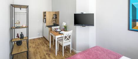 A compact room with a bed, a desk with a chair, a TV, and a shelf unit.