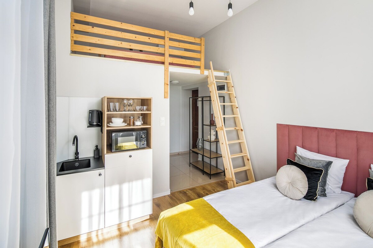 A compact bedroom with a bunk bed, a kitchenette, and a ladder leading to an upper bunk.
