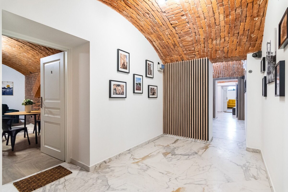 A hallway with a brick ceiling, white walls, and a marble floor. There are framed pictures on the wall and a wooden slat partition.