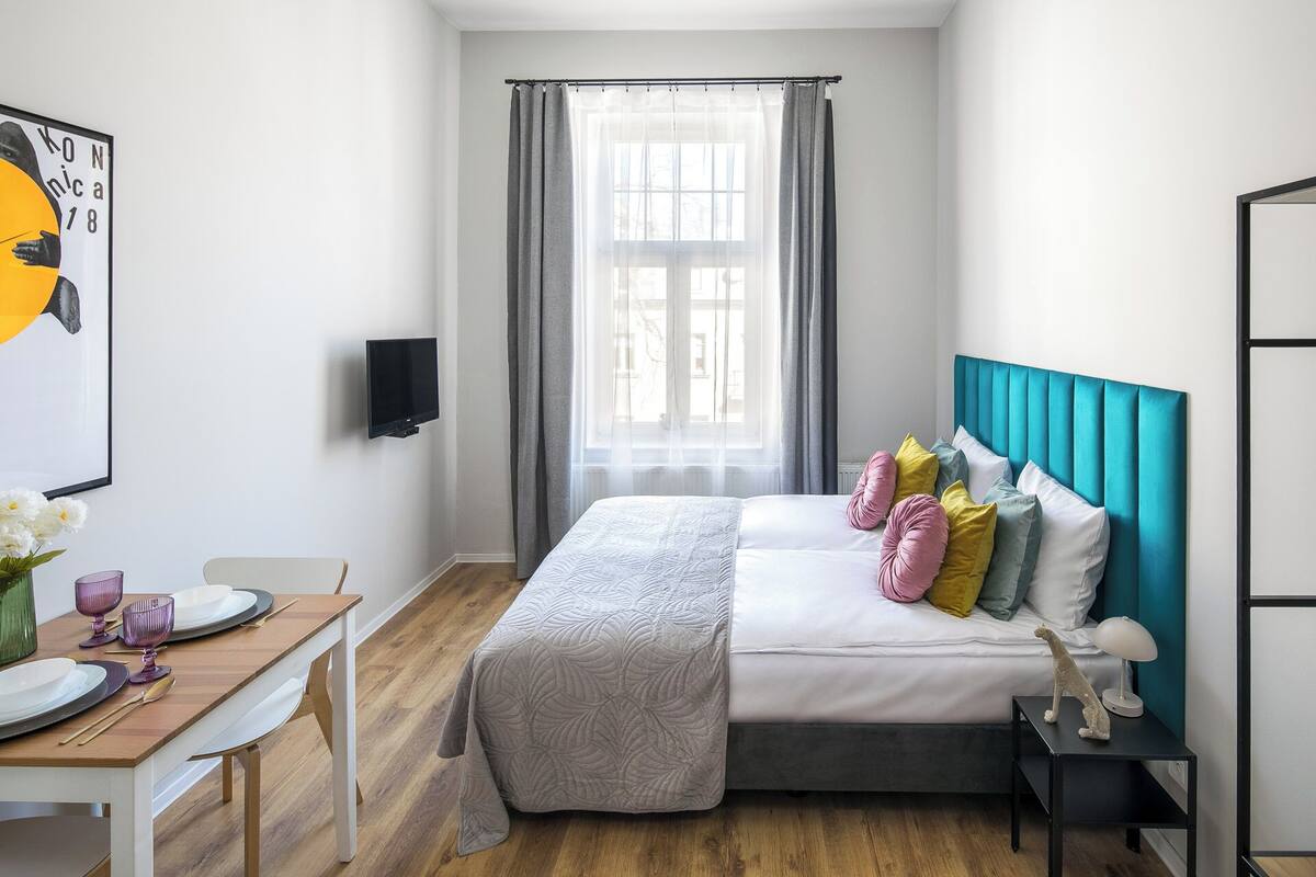 Un dormitorio moderno con cama, mesita de noche y ventana con cortinas.