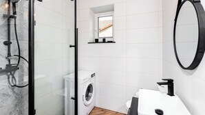 A modern bathroom with a glass shower enclosure, a washing machine, a toilet, and a large mirror. - Horizon Park Aparthotel (Kraków)