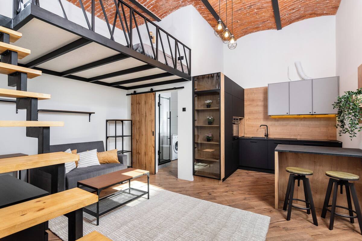 Un apartamento moderno estilo loft con una escalera, zona de estar, cocina y lavandería a la vista.