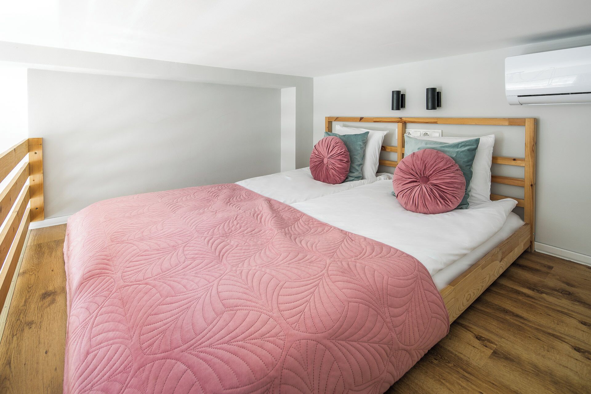 Ein Schlafzimmer mit einem hölzernen Bettgestell, weißer Bettwäsche und einer rosa Steppdecke.