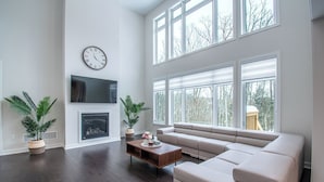 A modern living room with a fireplace, large windows, and a comfortable seating area. - Twilight Pines - Four Bedroom Cottage, Sleeps 8 (Huntsville)