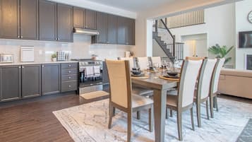 A modern kitchen with dark cabinets, a built-in oven, and a dining area with a wooden table and chairs.