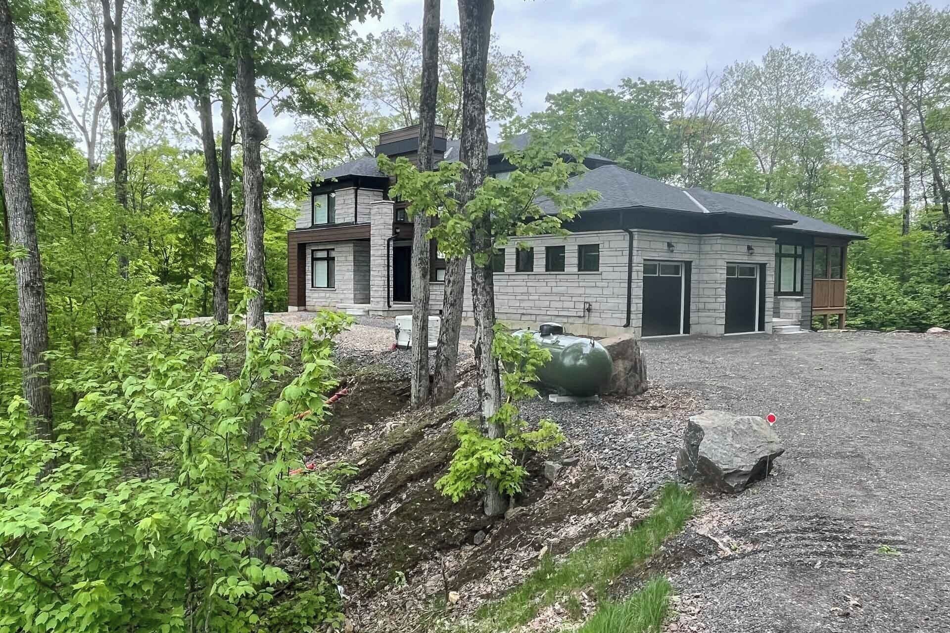 Une maison moderne à deux étages, dotée d’une façade en pierre et entourée d’une forêt dense.