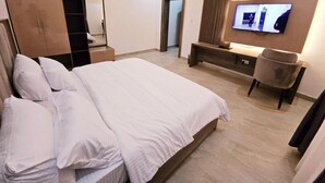 Et hotelværelse med en stor seng, et klædeskab, en bænk, en stol og et TV ophængt på væggen.