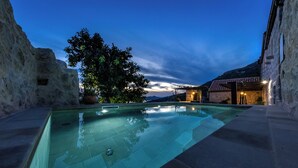 A swimming pool with clear water, surrounded by stone walls and a tree.