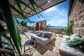 A covered outdoor seating area with stone flooring, a sofa, and a table with a laptop.
