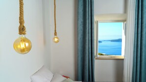 A bedroom with a bed, a hanging light fixture, a window with curtains, and a view of the sea.
