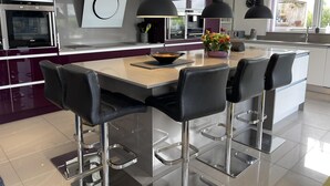 Una cocina moderna con una isla central, taburetes de bar, iluminación colgante y electrodomésticos de acero inoxidable.