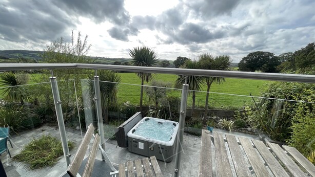 Un balcón con jacuzzi, terraza de madera y vista a un campo verde.