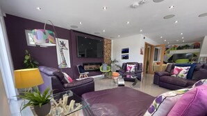 Una sala de estar moderna con un sofá morado, una mesa de centro de vidrio y un televisor montado en la pared.