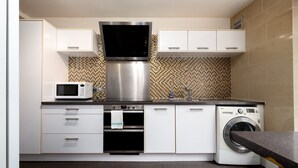 Una cucina moderna con mobili bianchi, una cappa in acciaio inossidabile, un forno a microonde, un forno, un lavello e una lavatrice integrata.