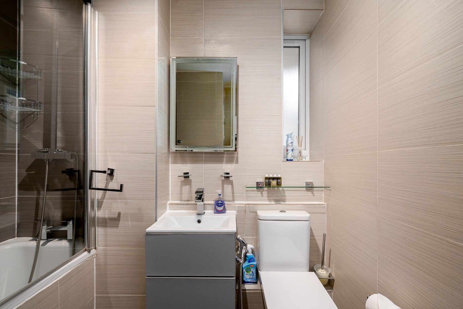A modern bathroom with a glass shower enclosure, a white sink, a toilet, and a mirror above the sink.