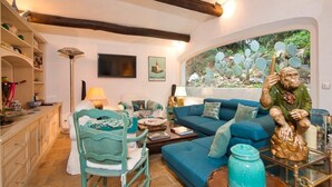 A cozy living room with a blue sofa, a green chair, and a decorative statue. - Villa with swimming pool walking distance from the beach (Ramatuelle)