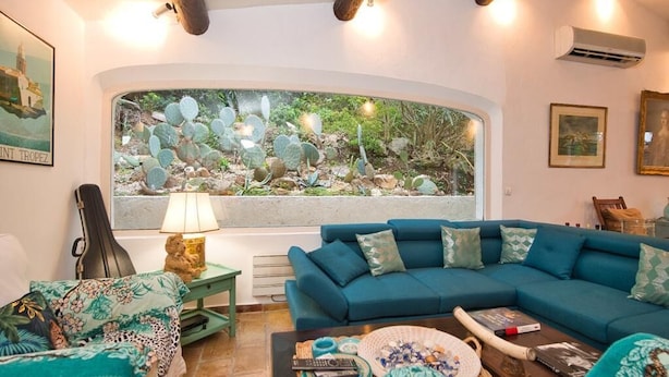 A living room with a large window, a blue sofa, a small table, and a guitar. - Villa with swimming pool walking distance from the beach (Ramatuelle)