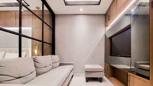 A modern living room with a sofa, ottoman, and a flat-screen TV mounted on a wooden cabinet. - Modern Sophisticated 1Br At The Smith Alam Sutera Apartment (Tangerang)