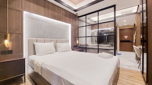A modern hotel room with a large bed, a wooden headboard, and a glass partition separating the room from the dining area. - Modern Sophisticated 1Br At The Smith Alam Sutera Apartment (Tangerang)
