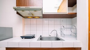 A kitchen with white tiles, a stainless steel sink, a wooden cabinet, and a Modena range hood. - Nice And Wonderful Studio At Margonda Residence 2 Apartment (Depok)